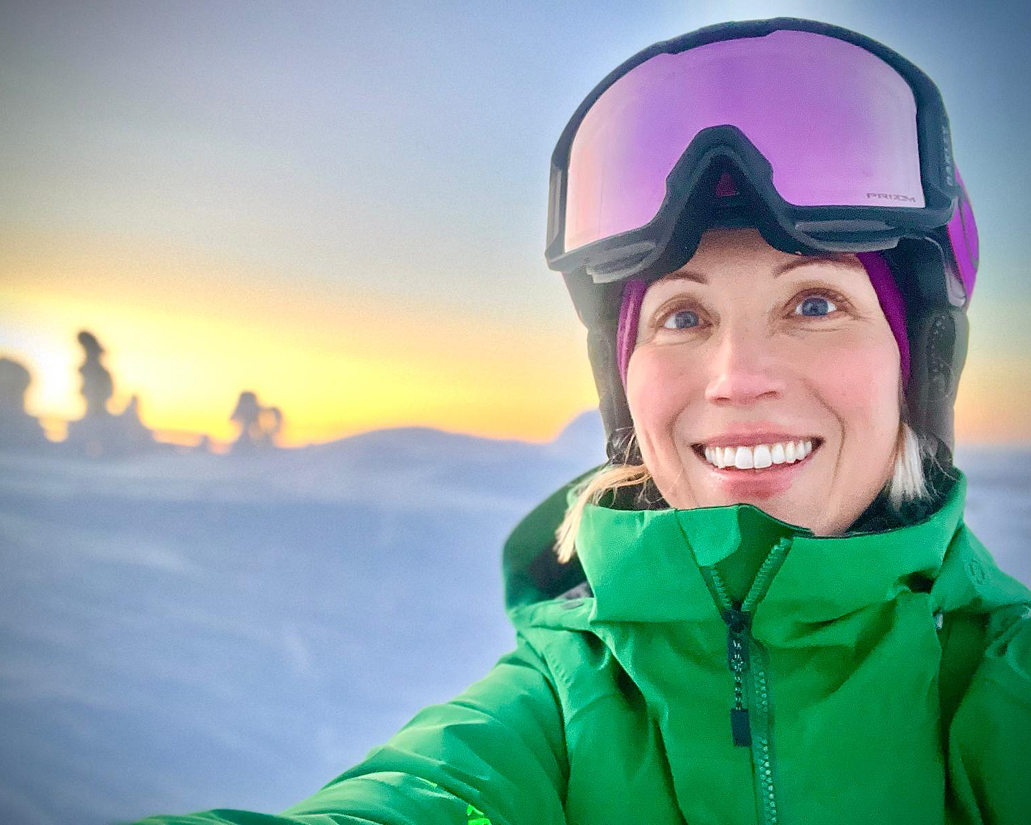 Grannas lähikuvassa laskettelurinteessä, kypärä päässään ja laskettelulasit otsalle nostettuna. Taustalla hehkuu auringonnousu. 